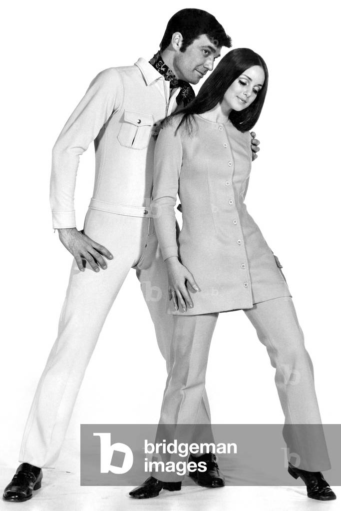 Clothing. John and Shirley are ready to go in Jersey. His beige Swedish stretch jump suit, in zipped-up battledress style, costs 20 guineas, from Just Men, London, SW3 Her bright canary-yellow pants suit has a flare-line button-through top which can be worn as a mini coat-dress. Price £10 at Mates, Oxford Street, London. January 1969