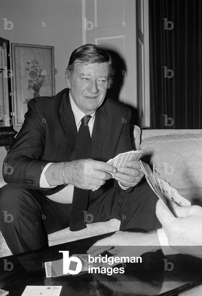 John Wayne pictured relaxing playing cards in his suite at The Connaught Hotel, Mayfair, London. January 1974.