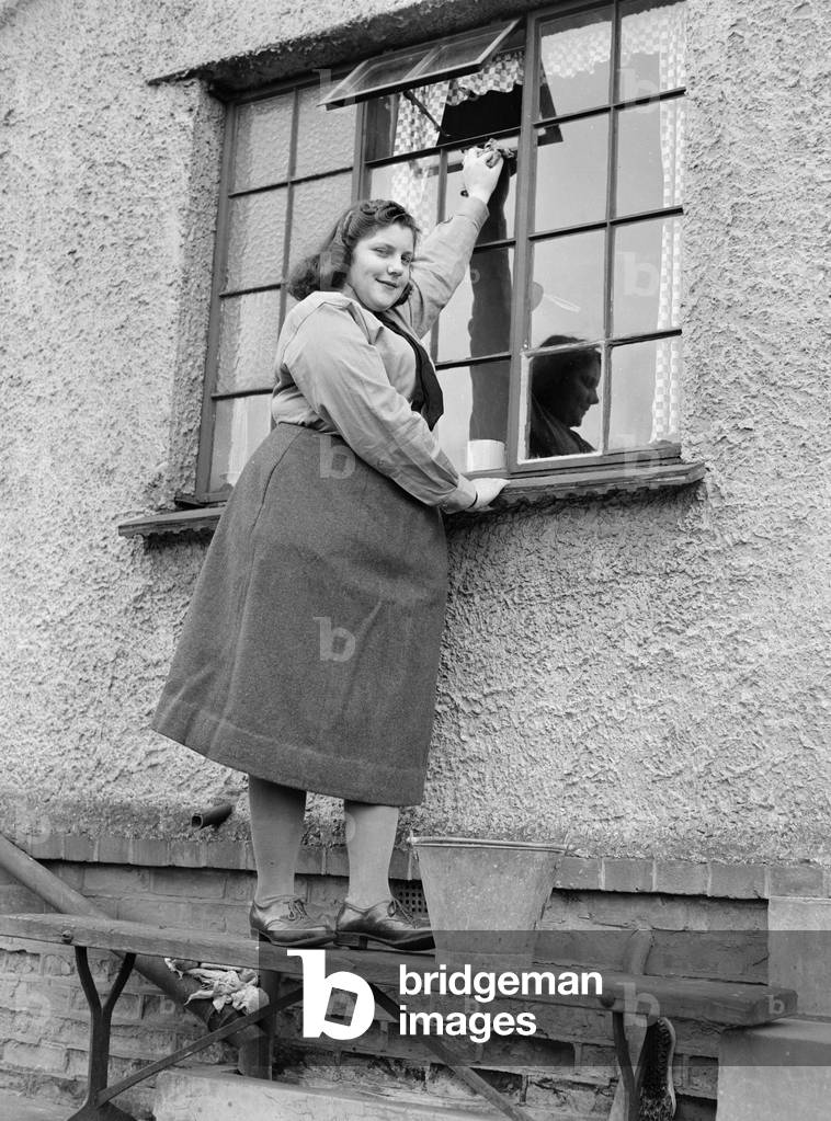 A busy housewife cleaning her windows at home, c. 1954 (b/w photo)