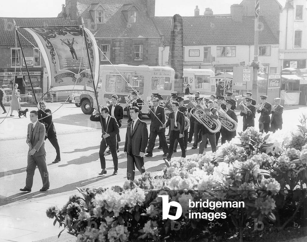 Banner fluttering in the breeze and band playing lustily, Bedlington Dr Pit branch, March through the town, past the first of the armada of ice cream vans, June 1962 (b/w photo)