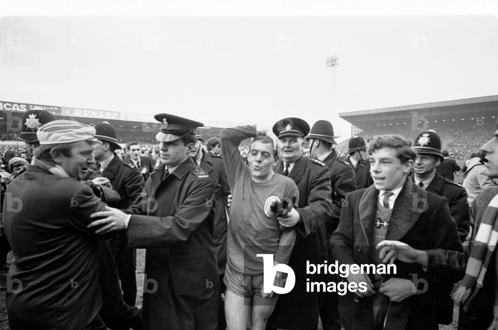 FA Cup Semi Final match at Villa Park. Liverpool 2 v Chelsea 0. Liverpool footballer Ian St John protected by policemen as fans run onto the pitch to celebrate their team's victory. 27th March 1965 (photo)