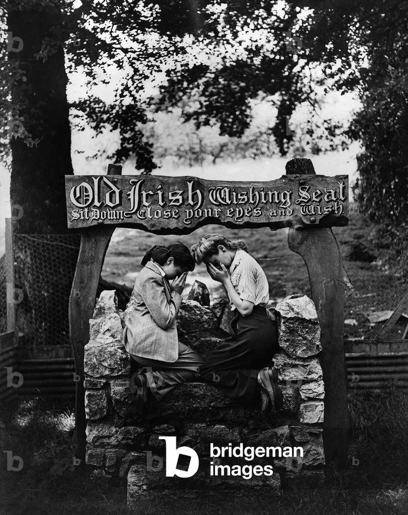 It Might come true! If, as the popular song says Wishing will make it so the dreams of these girls should come true in such a setting. The ancient Irish Wishing Seat has been transplanted in Primley, near Paignton, Devon, and for a few pence, you can sit in it and make your wish, but no money is refunded if results are not forthcoming. The girl on the left has a brother in Merchant Navy, and the girl on the right has her husband in the Middle East, so it's not difficult to imagine what their wishes are unless their wishes take in the world issues of today. August 1943 (b/w photo)