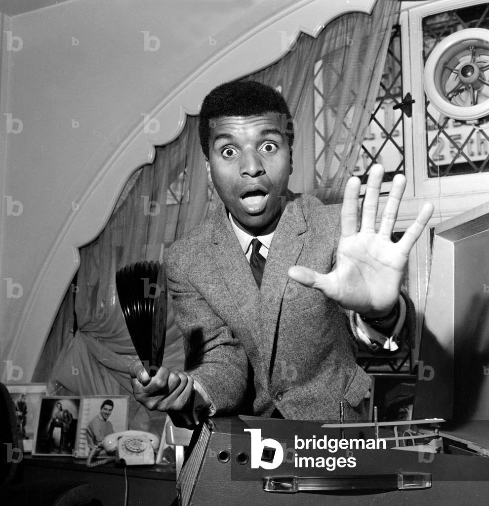 Singer and Comedian Kenny Lynch seen here with his latest record to gain entry into the top thirty, July 1963 (b/w photo)