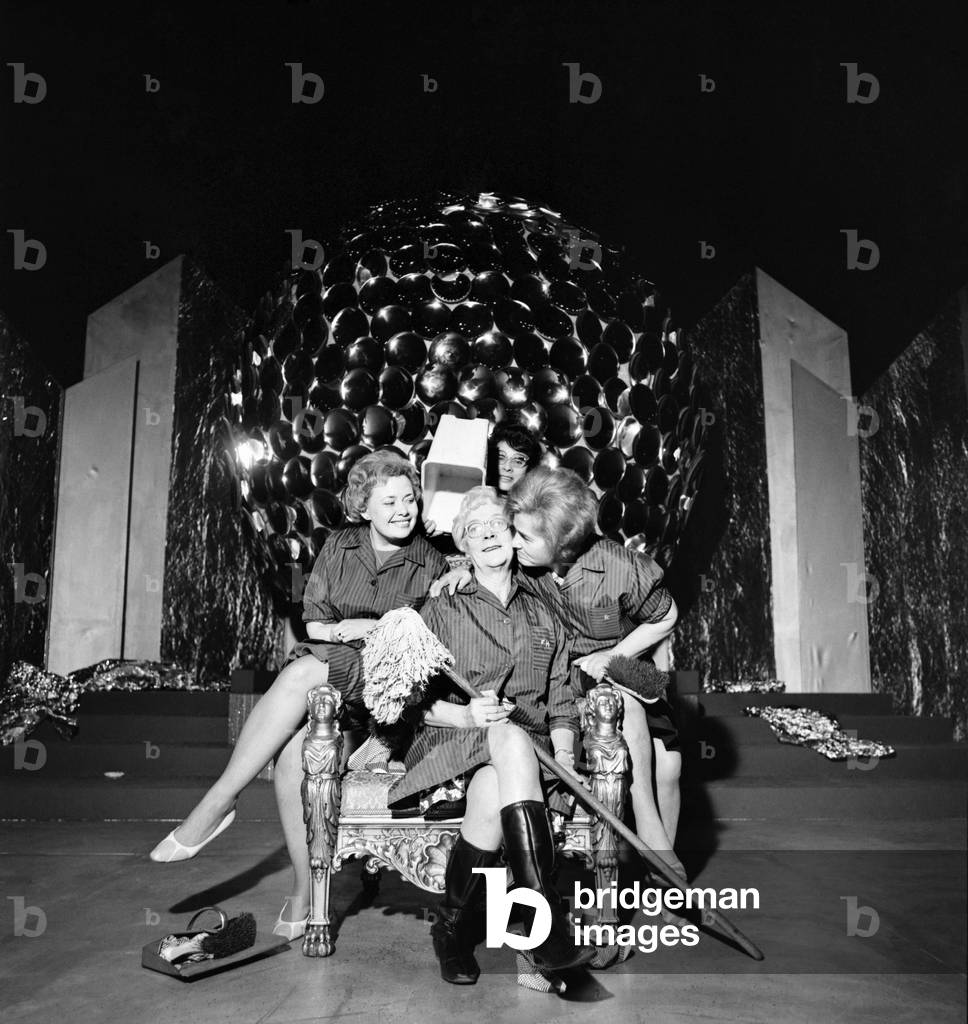 If only I were younger! Mrs. Florence House of Battersea could not resist the temptation of sitting on the throne which the Miss World contestant (winner) will sit in tomorrow night at the Royal Albert Hall. Flo in one of the several women cleaners who go in daily to the Royal Albert Hall. Mrs. Florence House sitting on the Miss World throne complete with bucket (crown) and mop, with her two runners-up, (left) Mrs. Jean Cave from Battersea, and (right) Mrs. Trudi Lockwood from Barnes. Also pictured at the back is Mrs. Marty Hamilton from Notting Hill. November 1969