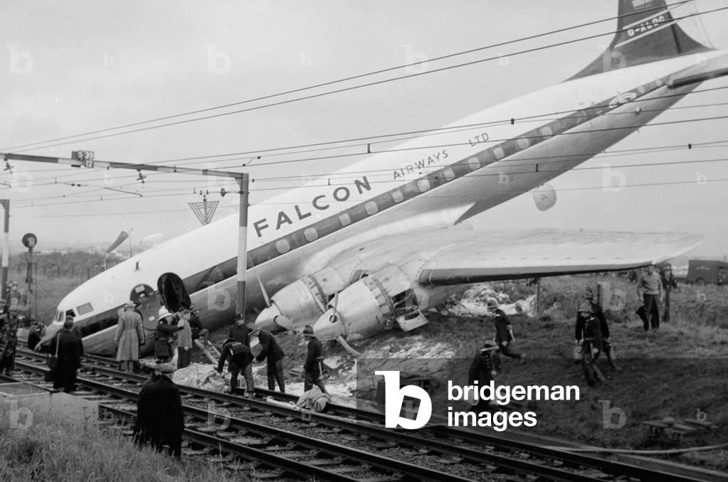 The wreckage of a fully-laden passenger Viscount aeroplane after it had overshot the runway at Rochford Airport and ended tail up on the railway line which runs alongside the airport. 
Firemen and emergency services clear the way for passengers to exit the plane, October 1960