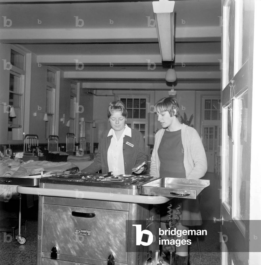 17 year old Kathryn Beckett and 18 year old Wendy Booth (both of Rhyl) remove a meal Trolley from one of the wards. December 1969