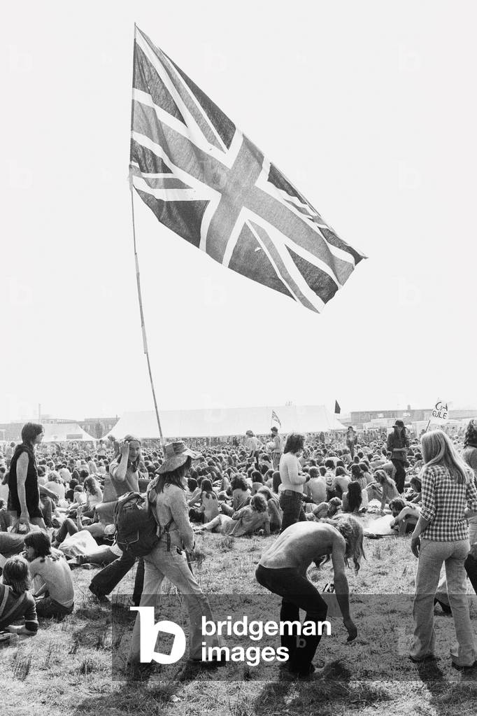 Reading Pop Festival. Young festival goers carrying the Union Jack flag as they make their way to the main stage, 24th August 1973 (b/w photo)
