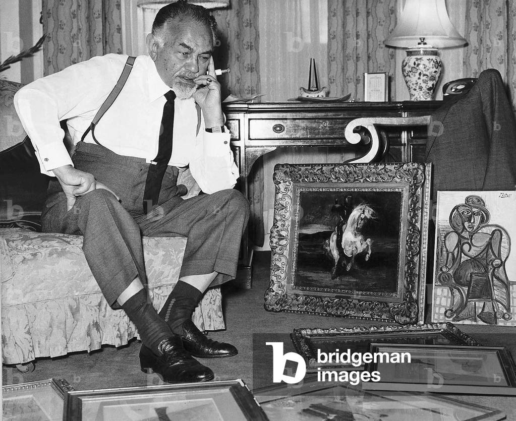 Edward G Robinson takes a seat as he views a collection of art paintings loaned to him from Sotheby's in his hotel room, 1966 (b/w photo)