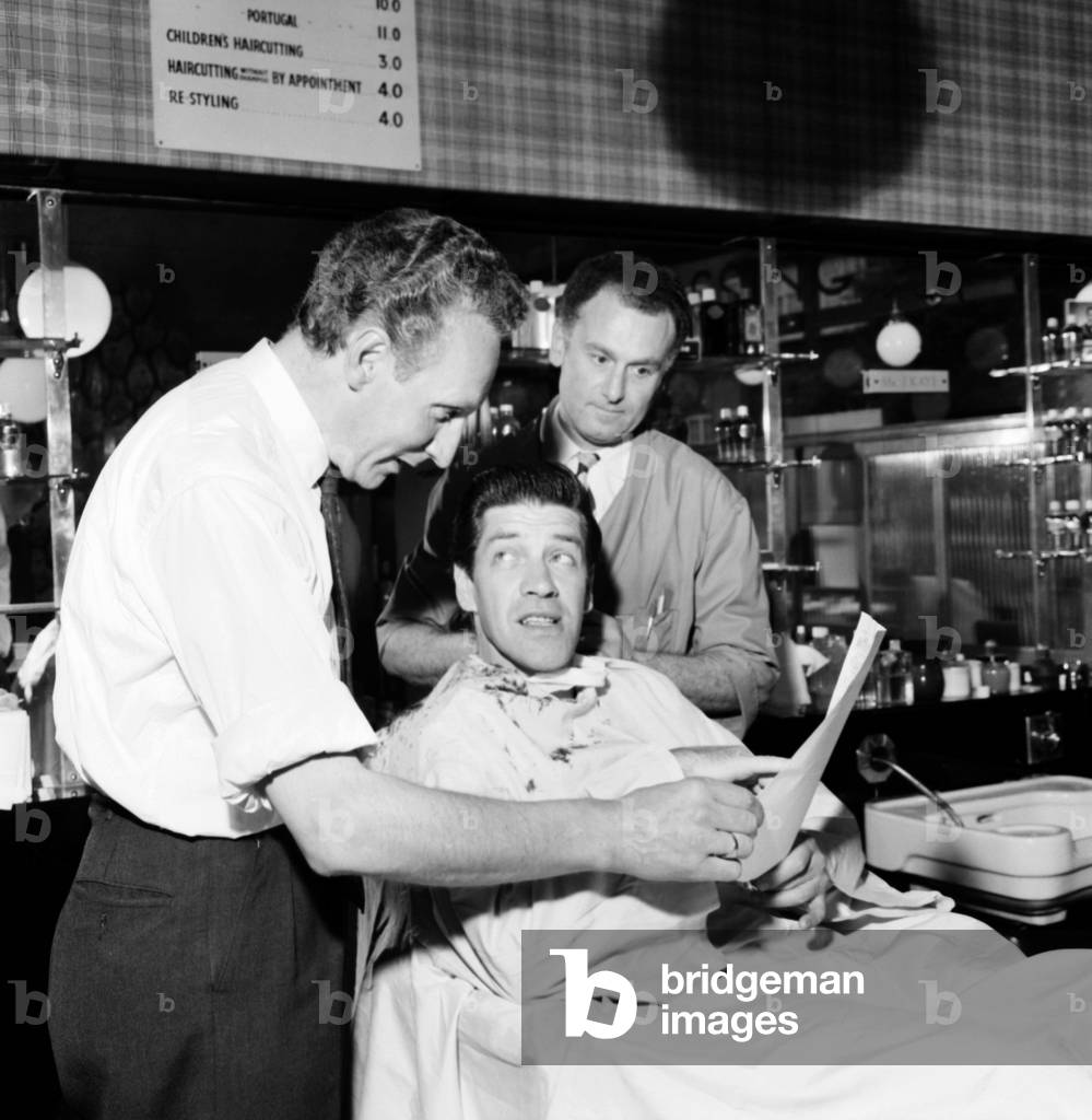 Barber Shop: Michael Holliday having hair cut at Ronnies of Streatham. Sidney Hayman, aged 45, of Pullman Court, Streatham, was pop singer Michael Holliday's regular barber until about 2 year ago when he moved to a different shop and Michael Holliday lost track of him. Later Michael Holliday phoned for an appointment at Ronnies, Leigham Road, Streatham, where Sidney is now working, and went down there two hours later with his son Michael Agedio, from their home in Bishops walk, Addington, for a reunion and better hair cut. June 1960