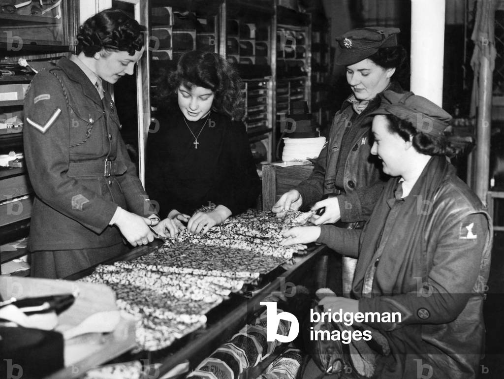 World War II Women: L/Cpl Joy Barber measuring out a length of cloth behind the counter. Teaching her is 15-year old Anne White. The customers are Cpl. Mary Newman and Pte. Philomena Waterhouse. January 1946