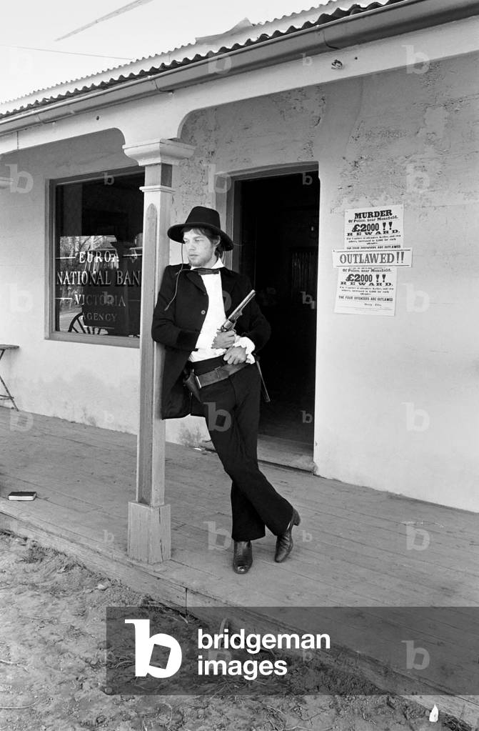 Rolling Stones: Filming Ned Kelly in Australia. Mick Jagger. Mick Jagger with gun on the verandah of the bank. July 1969