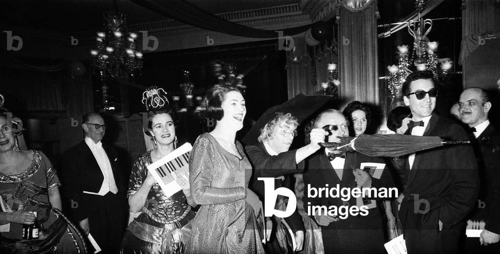 George Henry Hubert Lascelles, 7th Earl of Harewood, & Countess of Harewood attend the Opera Ball at the Dorchester Hotel. Lord Harewood, dressed in a clergyman's outfit, points with his brolly. On left is Joan Sutherland, far left, Lady Harewood, February 1960 (b/w photo)