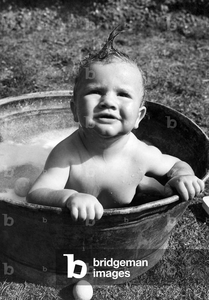 Young toddler having a wash in a tin bath in the back garden in Erith, Kent. 
July 1943