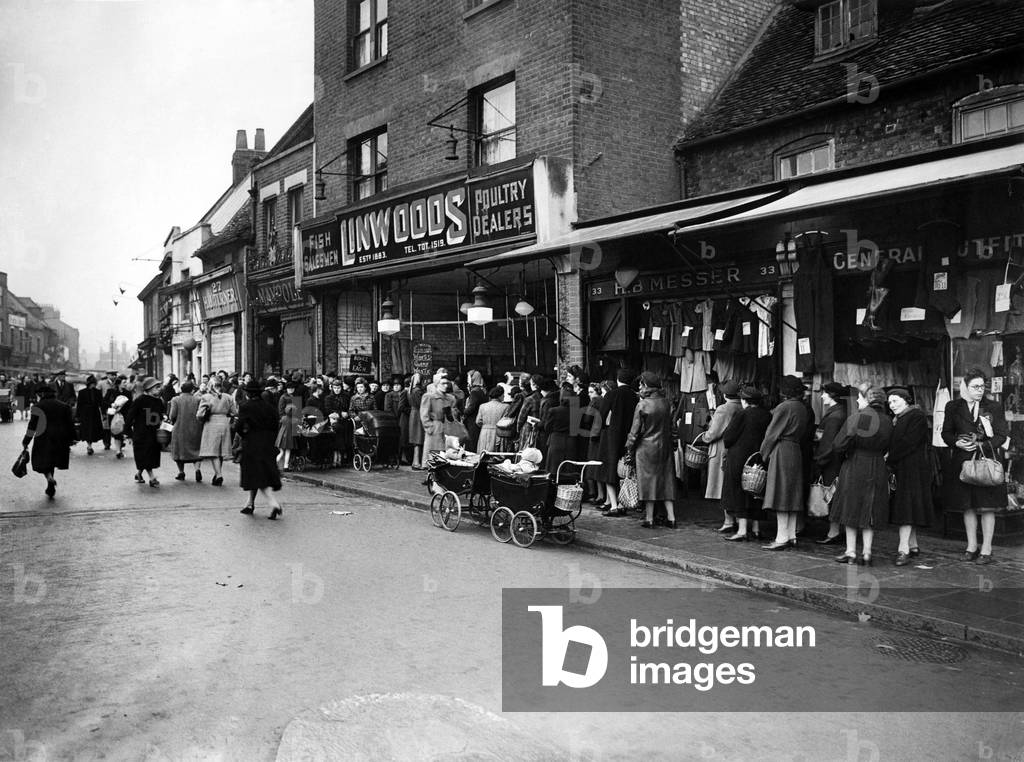 This shop in North London has got the goods and organises the sales end so that two queues can be dealt with at the same time as one. Prams are parked in the road. 1946 P018774
