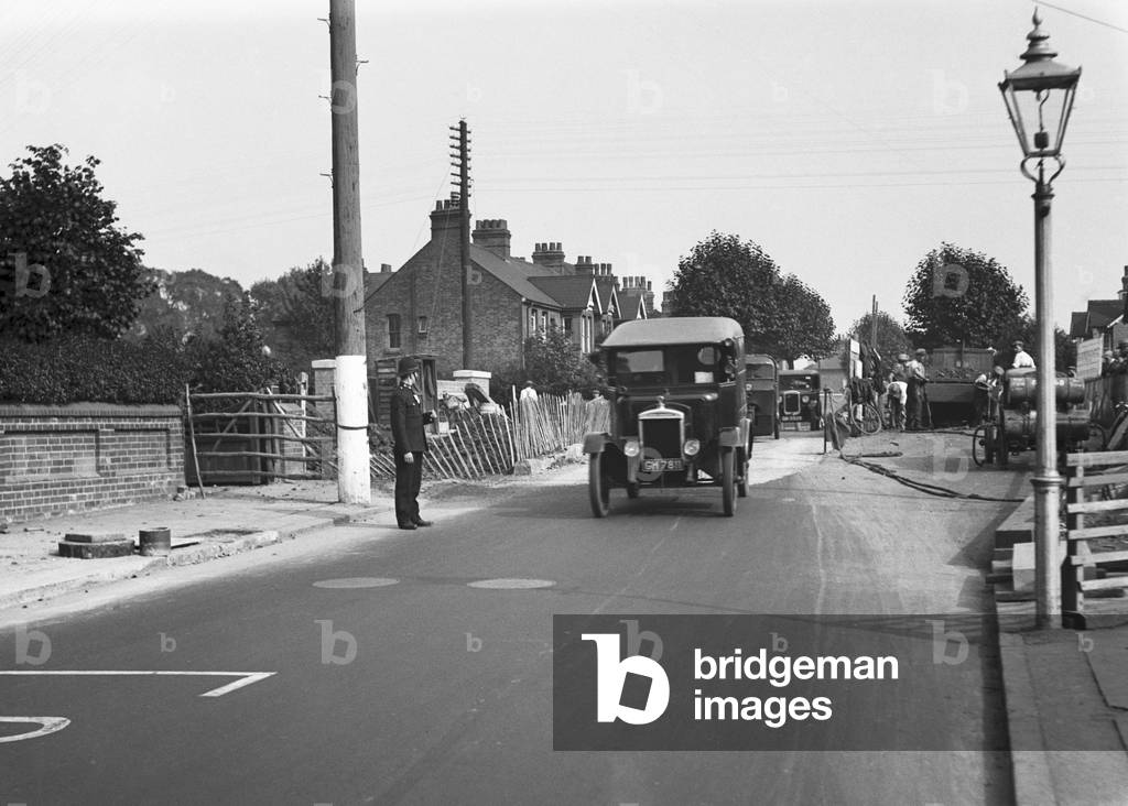 Police direct traffic as workmen repair the road in an unknown location in Uxbridge, London, c. 1931 (b/w photo)
