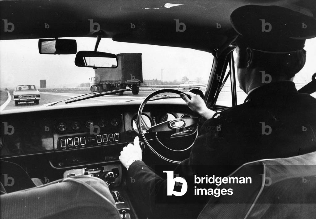 A police officer watching the traffic in his police car, c.1970