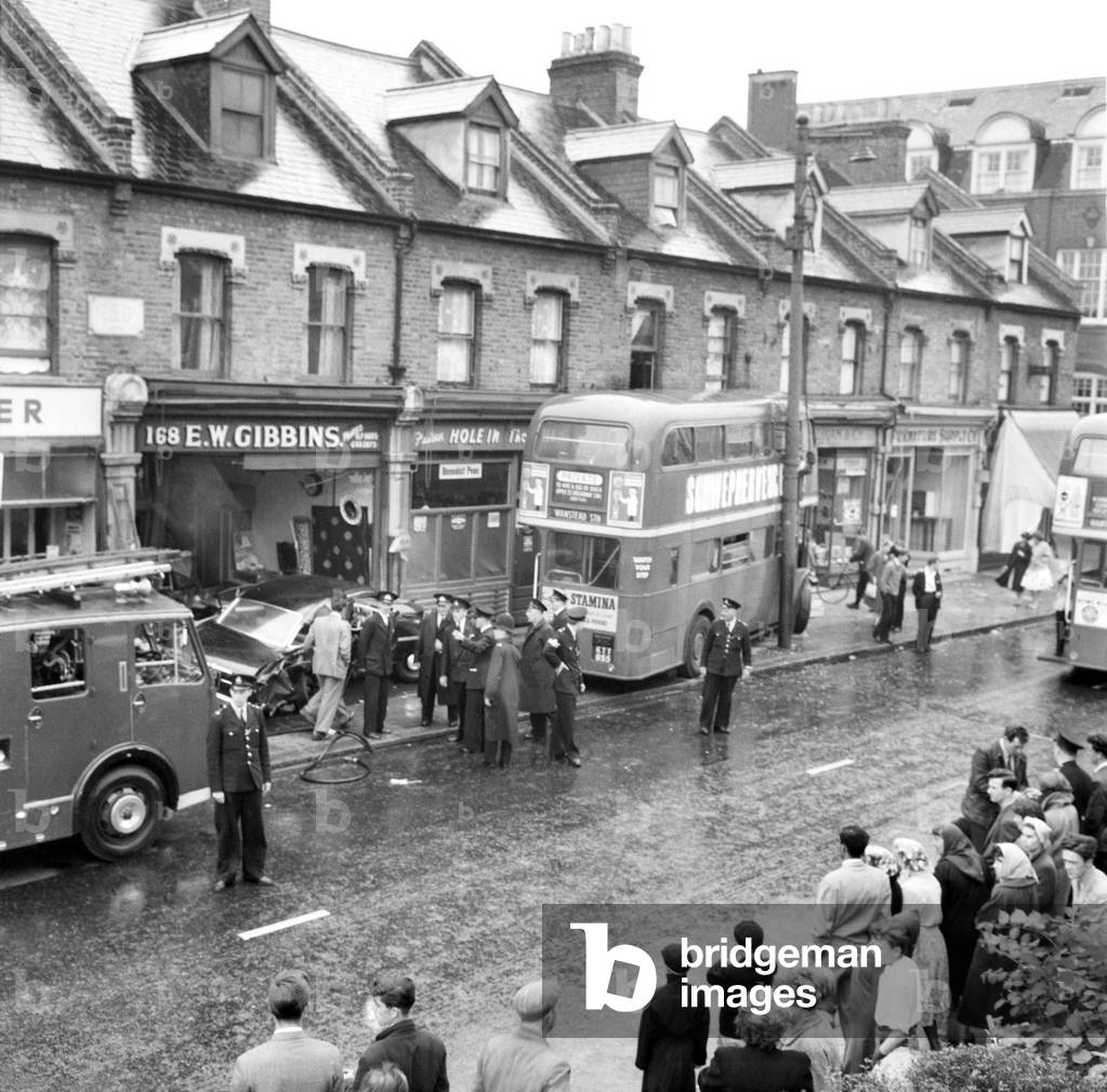 London Transport officals inspect the damage following a crash at Green Street, Upton Park. were 2 cars and a bus were involved in a collision. The bus ended up in the front of a shop . June 1960