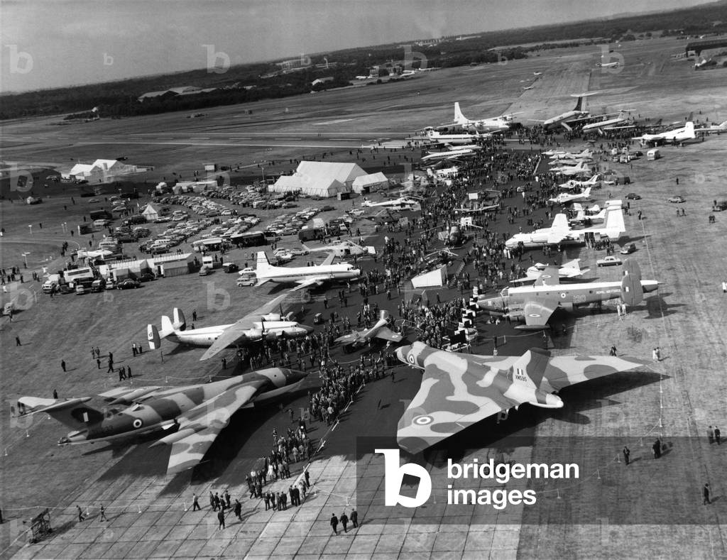 Farnborough air show opens after two-year break. A birds' eye view of the Farnborough Show - the first for two years - taken from a Westland Widgen helicopter. The camouflaged aircraft in the foreground are, on the left , a Victor, and on right, a Vulcan. Next to the Vulcan stands an Ambassador. Behind the Vulcan is a Shackleton and then a Dove, September 1964 (b/w photo)