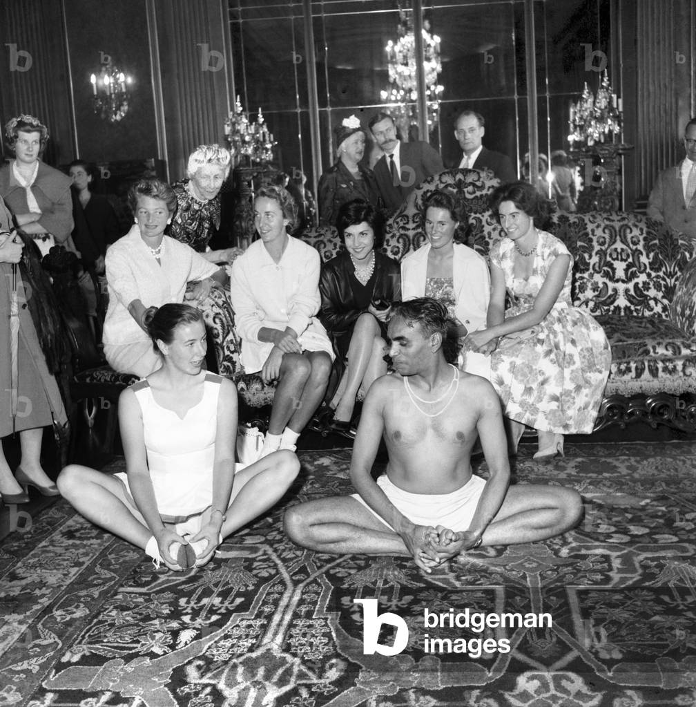 Yoga. Only the Centre Court would produce a similar nerve-racking moment for a tennis player...shakily trying a yoga exercise (above) is Carol Yates-Bell. Showing how it should be done is yoga expert Mr. Bombay Iyengar. They were at the pre-Wimbledon party given by Lady Crosfield at her Highgate home yesterday. Watching are (left to right) tennis stars Angela Buxton, Pat Hird, Shusha Asar, Gillian Evans and Pauline Roberts. June 1960