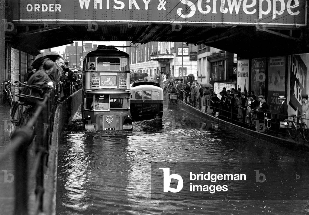 Alfieri. Flooding at Surbiton. Passers-by watch traffic go under a bridge. 19th April 1932 (b/w photo)
