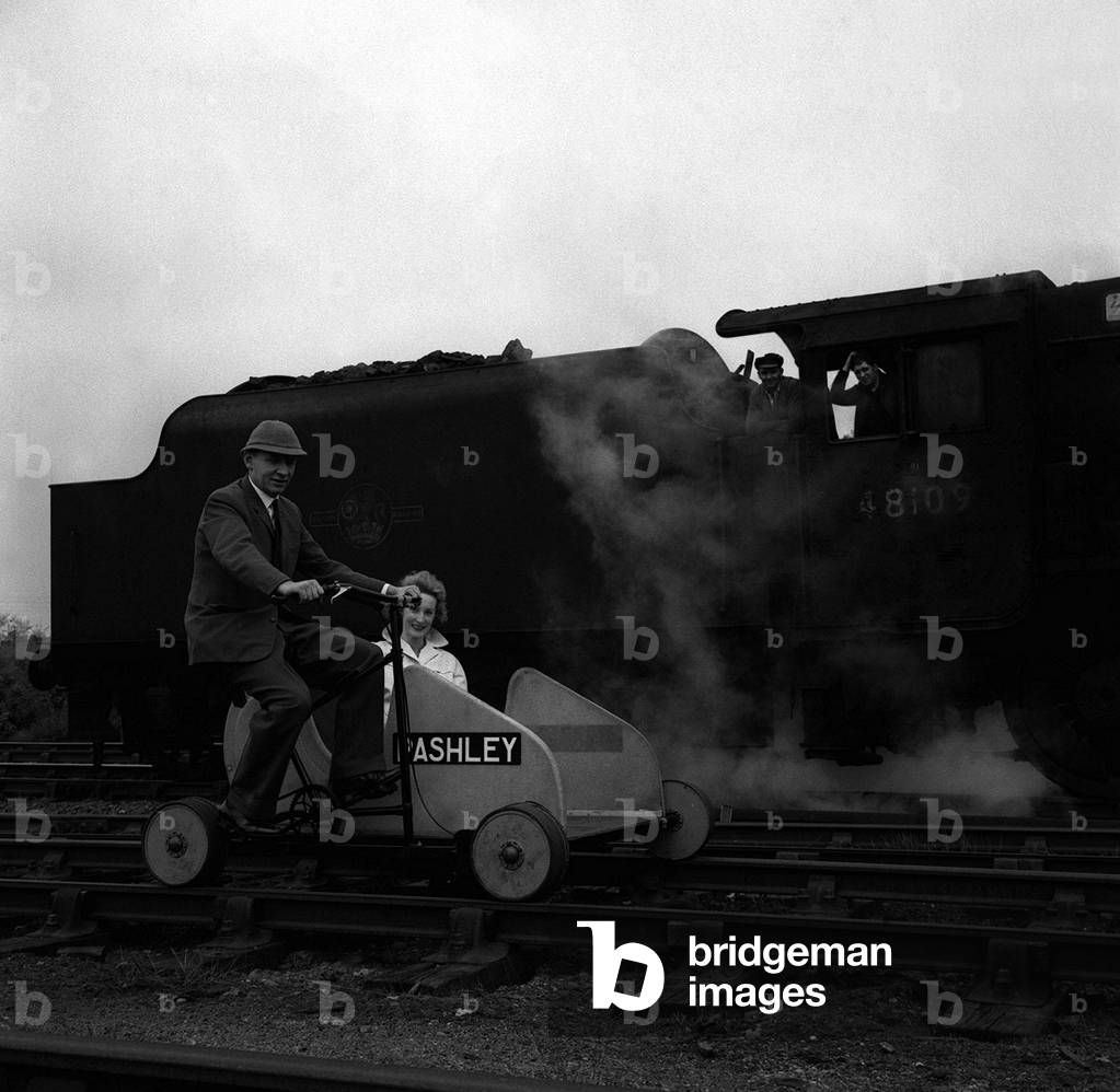 A rail quad cycle seen here over taking a stationary steam locomotive has the driver and the fireman scratching their heads in amusement, May 1963 (b/w photo)