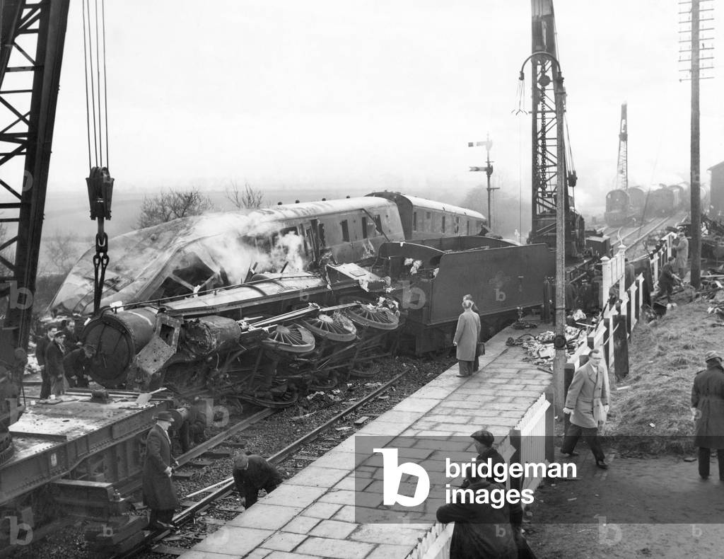 Baschurch train crash: The recover operation at Baschurch railway station following the collision between Wellington to Chester Down express passenger train and a freight train, which had been shunted into a siding for the passenger train to go ahead, which was still partially obstructing the main line. The locomotive of the passenger struck the leading vehicle of the freight train a glancing blow causing the passenger train to overturned on to the Up line between the platforms of the station. Three people were killed and 27 injured as a result of the accident. 13th February 1961 (b/w photo)