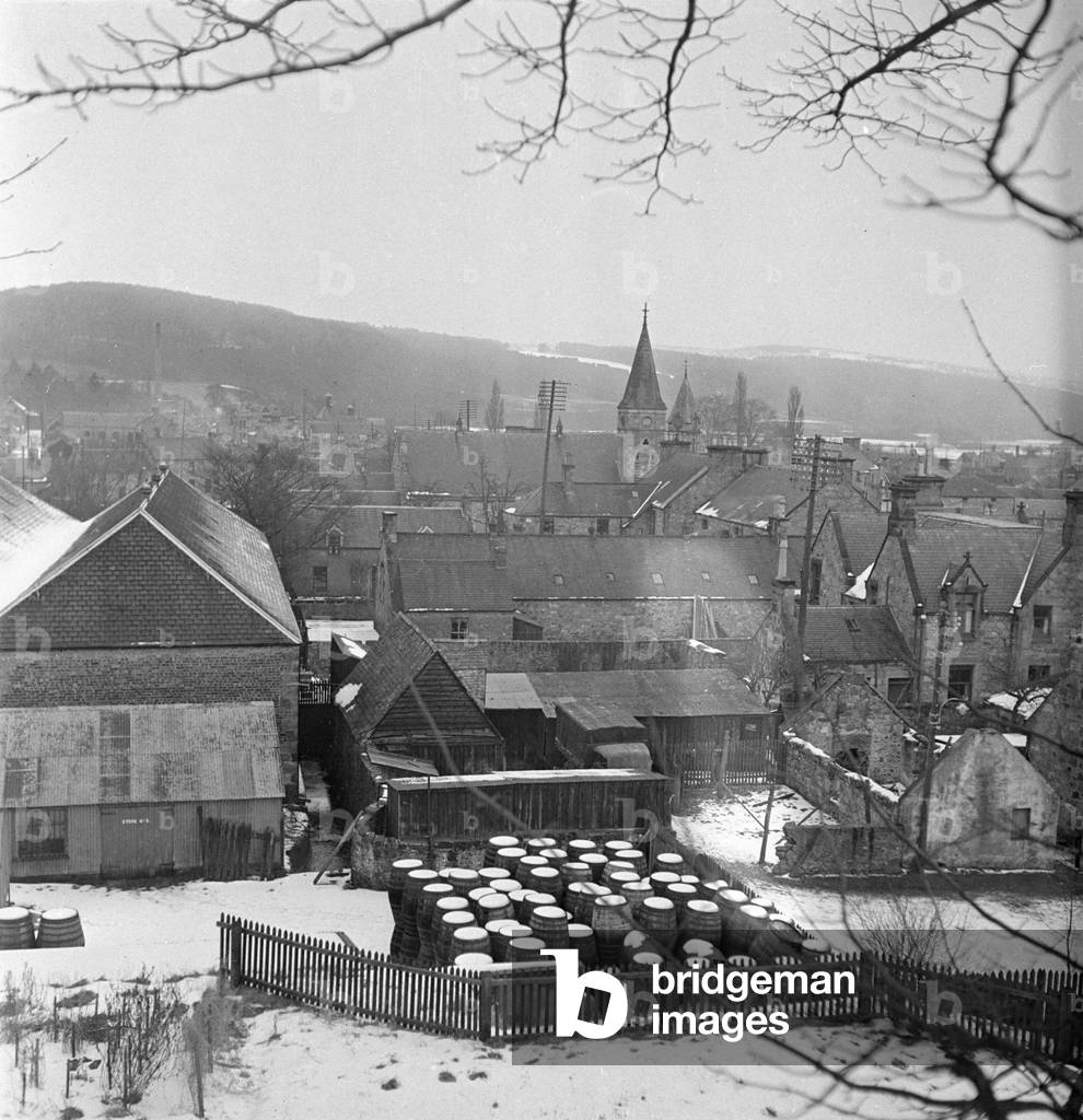 The barrel store for the Glen Grant Distillery in the Highland village of Rothes. The distintive roofs of the distillery can be seen at the end of the High Street, Circa 1947