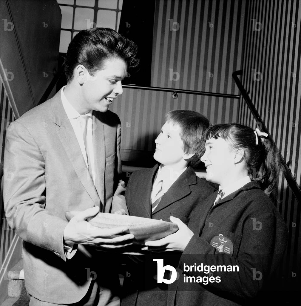 Singer Cliff Richard seen here presenting a school prize of three books to Carol Chamberlin at the Hugh Myddelton School as her friend Jean Arbuckle looks on. October 6th 1960 (b/w photo)