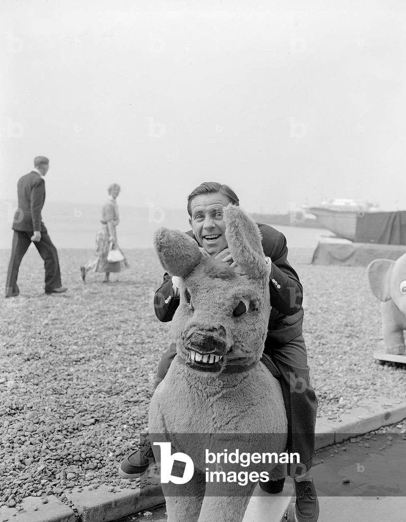Actor and comedian Norman Wisdom photographed on Brighton Beach on a stuffed donkey August 1955 (b/w photo)