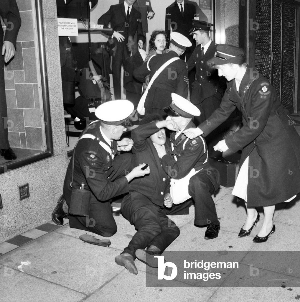 Ambulance men and medical workers attend to a Beatles fan who was injured in a crush as fans waited to get a glimpse of their heroes before the premiere of the film 'A Hard Day's Night' in Liverpool. 
July 1964