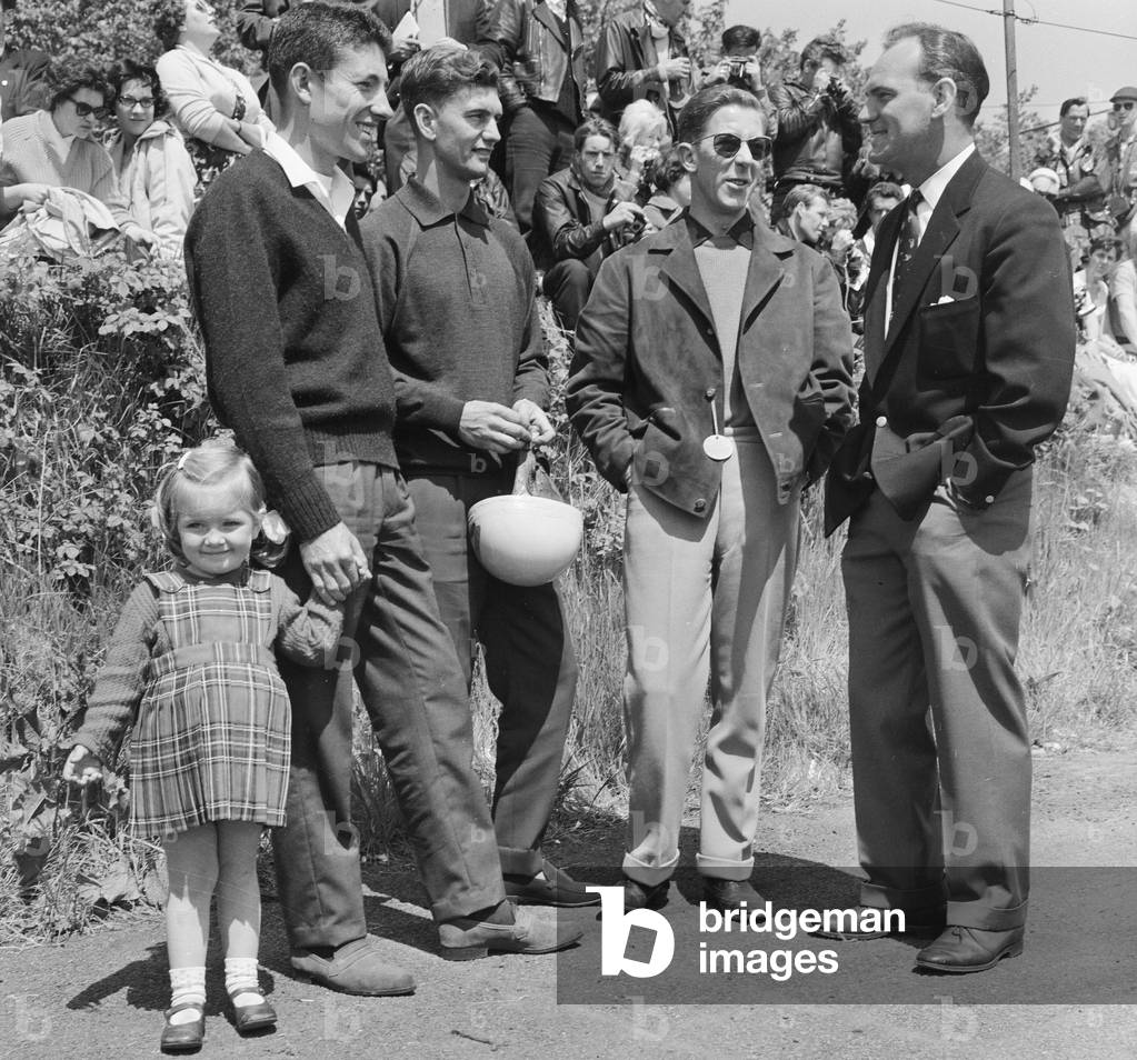 Debbie Phillis aged 3 daughter of Tom Phillis shows little interest as her dad talks shop with fellow riders Jim Redman, Armstrong and McCintyre. 4th June 1962 (b/w photo)