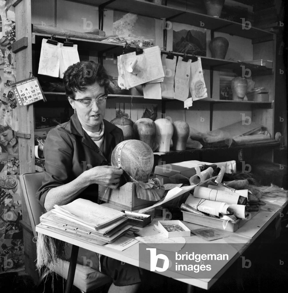 Wigmakers Workshop: Women making wigs whilst in another part of the workshop hair is selected for the next batch of wigs, November 1963 (b/w photo)