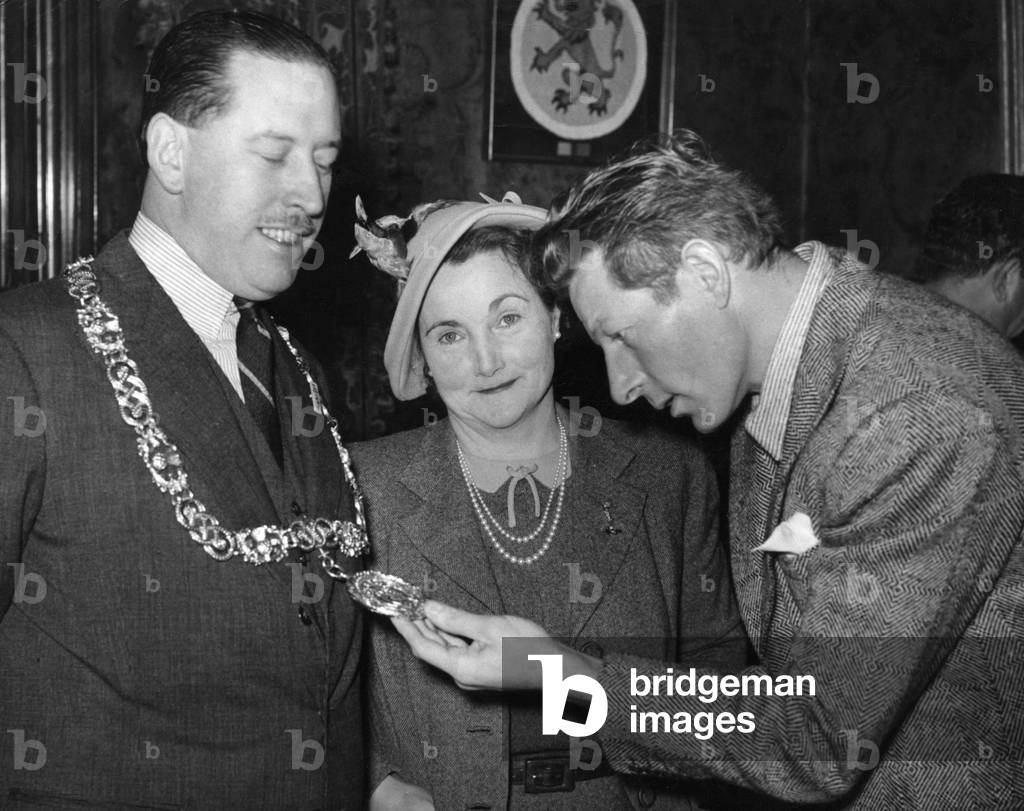 American actor and comedian Danny Kaye pictured with Lord Provost of Glasgow Victor Warren, admiring his chains of office as Lady Provost looks on at the City Chambers in Glasgow.7th June 1949 (b/w photo)
