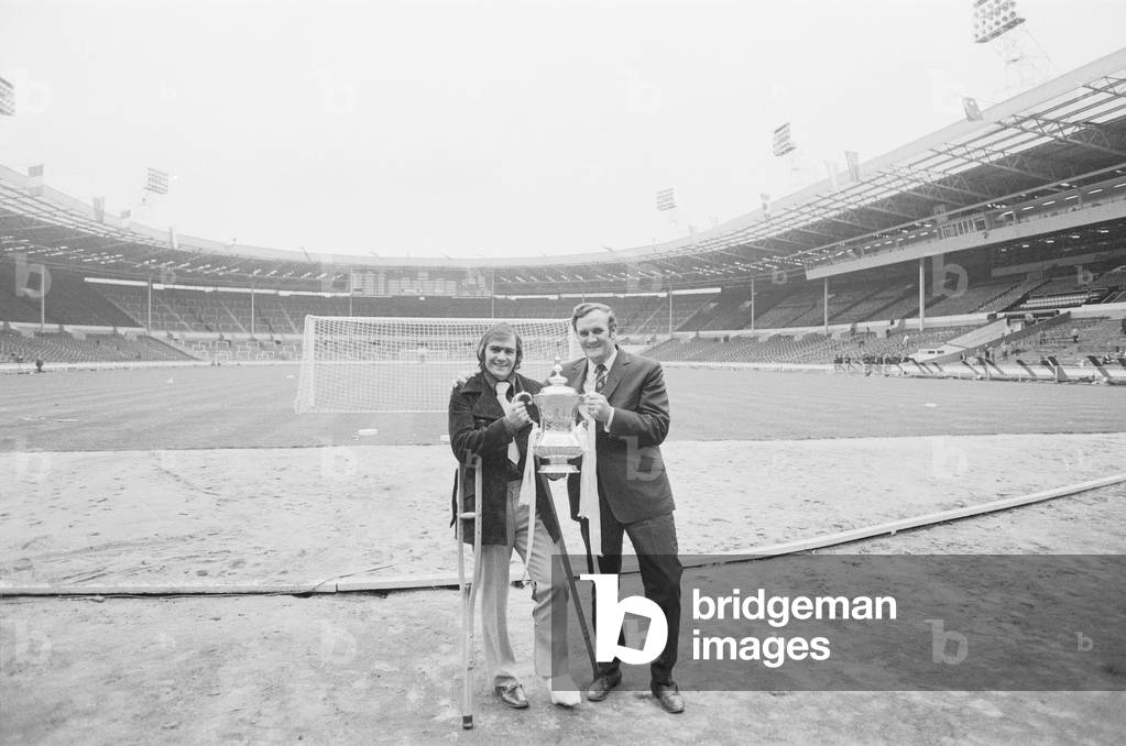 Don Revie poses with Terry Cooper and the F.A. Cup following Leeds United victory over Arsenal at Wembley. Cooper had suffered an horrific broken leg during a League game at Stoke City earlier in the year which meant him missing the FA Cup final. 7th May 1972 (b/w photo)