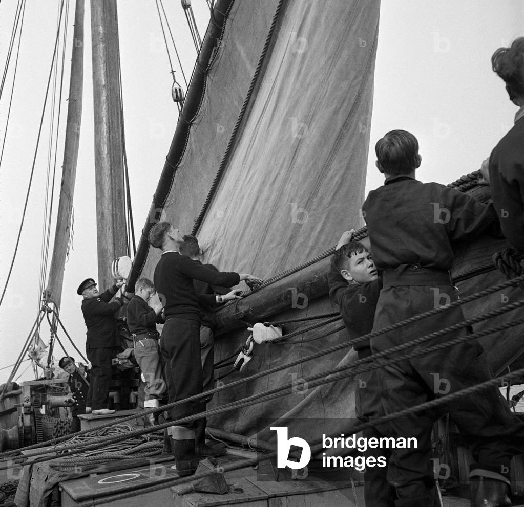Students attending the Outward Bound Sea School at Aberdovey seen here with one of the instructors unfurling a sail on the bowsprit of the school's schooner, October 1947 (b/w photo)