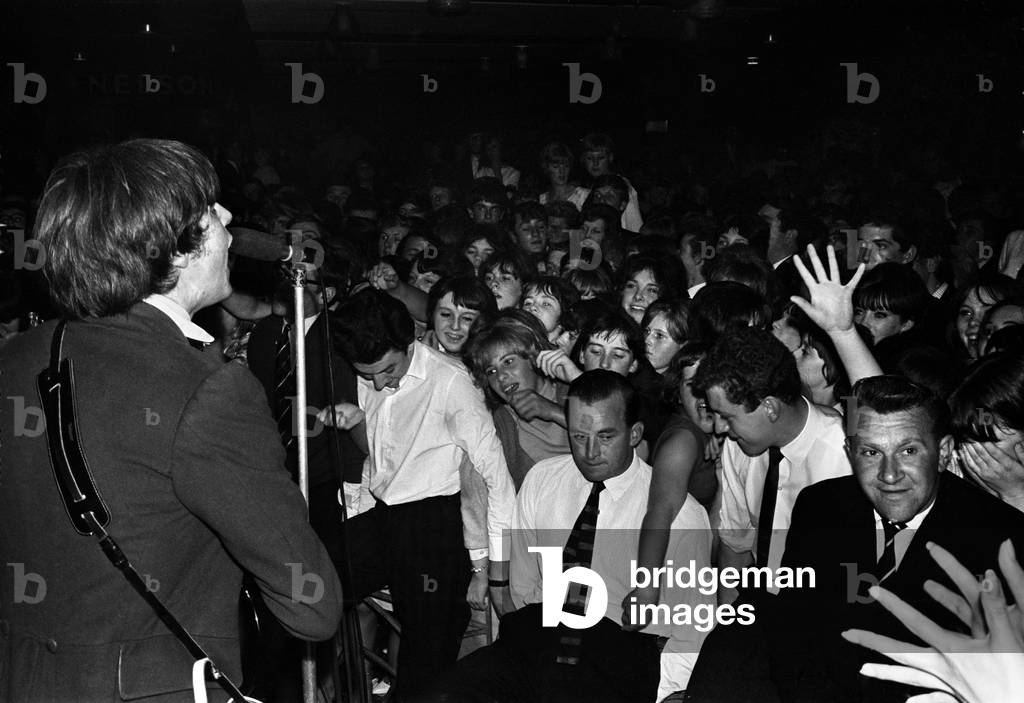 The Kinks on stage, singing to a large crowd
September 1964
