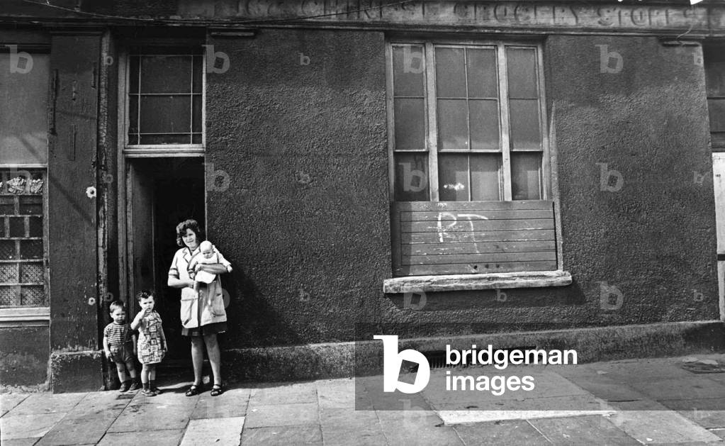 Mrs Yvonne Evans of Bute Street, Cardiff, with her children, Janet, aged 3, Stephen, aged 2 and Philip, three months, outside the condemned house in which she lives in by the docks of Butetown 
August 1969