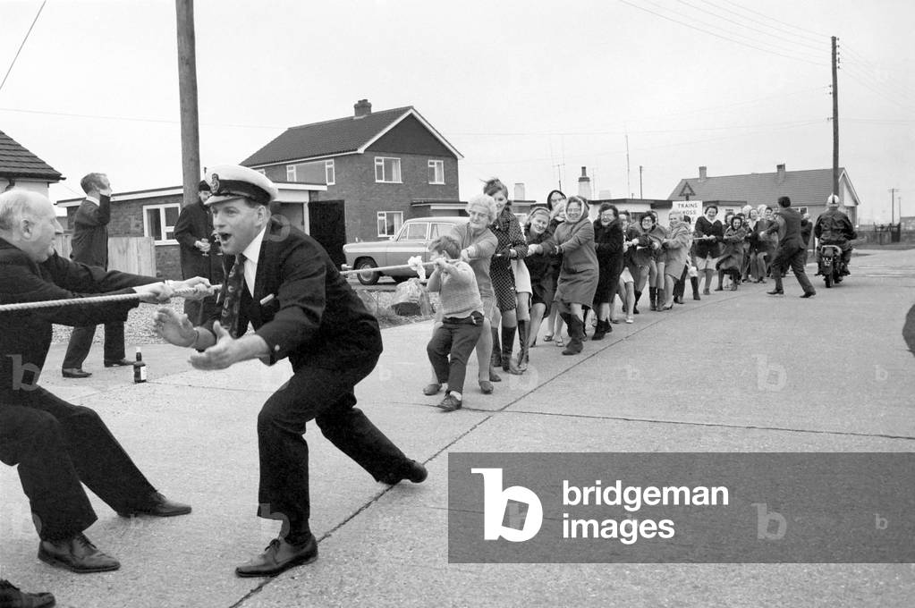 The annual Tug O' war battle of the sexes took place yesterday outside the Pilot Pub in Dungeness. Upwards of 100 people take place in this men v. women, no holds barred contest. The women won this years contest (the seventh) by winning two pulls out of three. Referee was Frank Paine, 32, Mechanic of the Mabel Holland, the Dungeness life- boat. Kent, December 1969 (b/w photo)