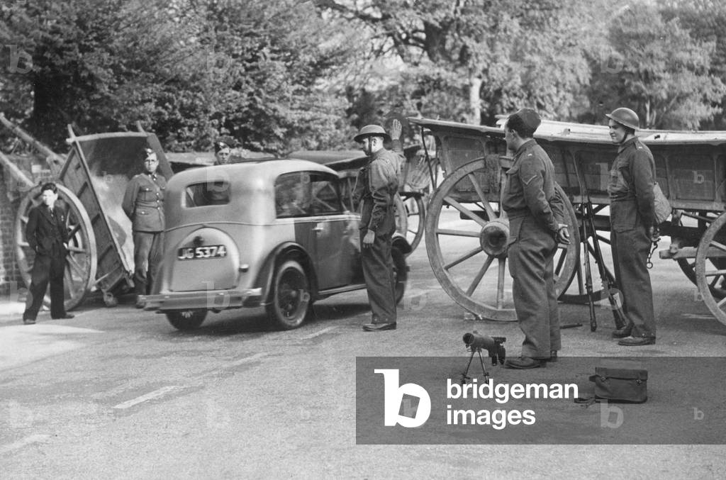 One of the many roads in England now closed off and protected by barricades and mounted machine guns during the Second World War. Cars are stopped and all identification cards have to be shown
 May 1940