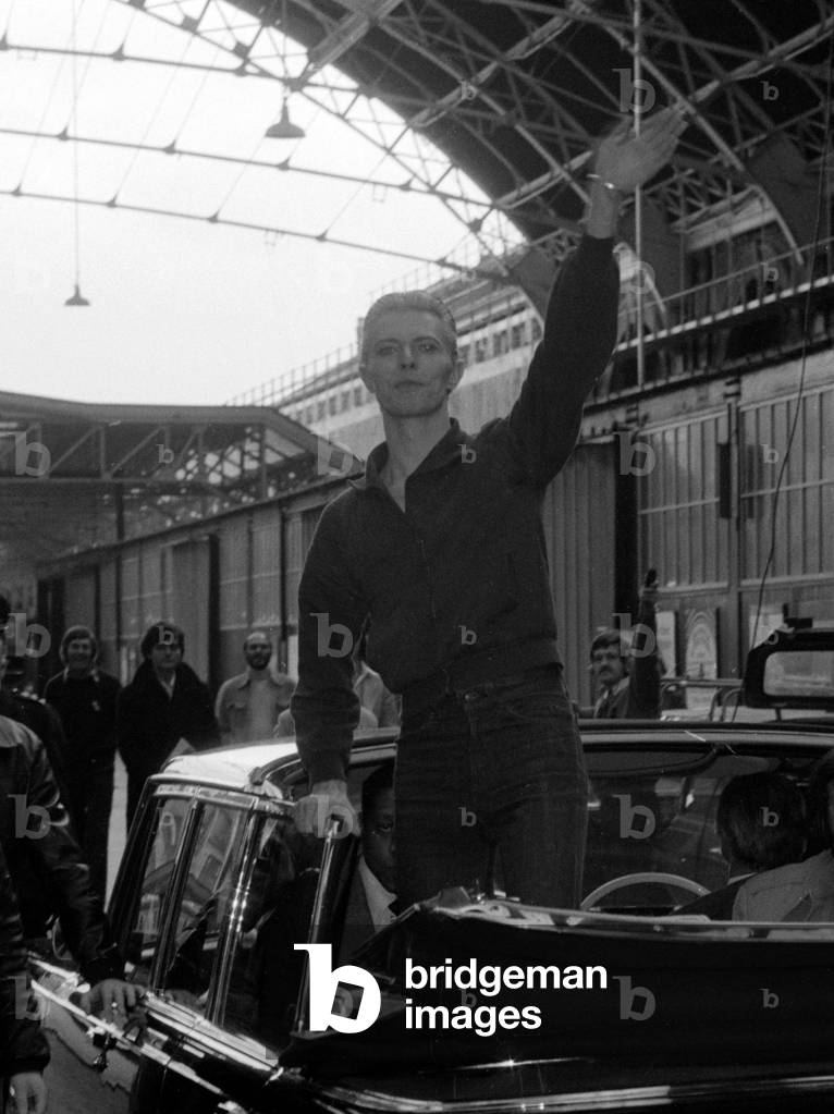 Pop singer David Bowie waves to fans as he arrives at Victoria Station May 1976 (b/w photo)