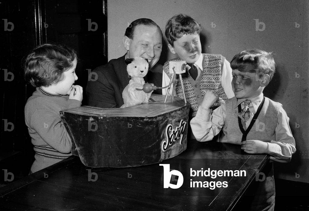 Harry Corbett and Sooty, the Teddy Bear Magician are seen here at home in Guisley, Yorkshire, with Corbetts two sons, Peter and David and their next door neighbour Joan Burtonwood. Peter and David have just received soot from a camera operated by Sooty, March 1954 (b/w photo)