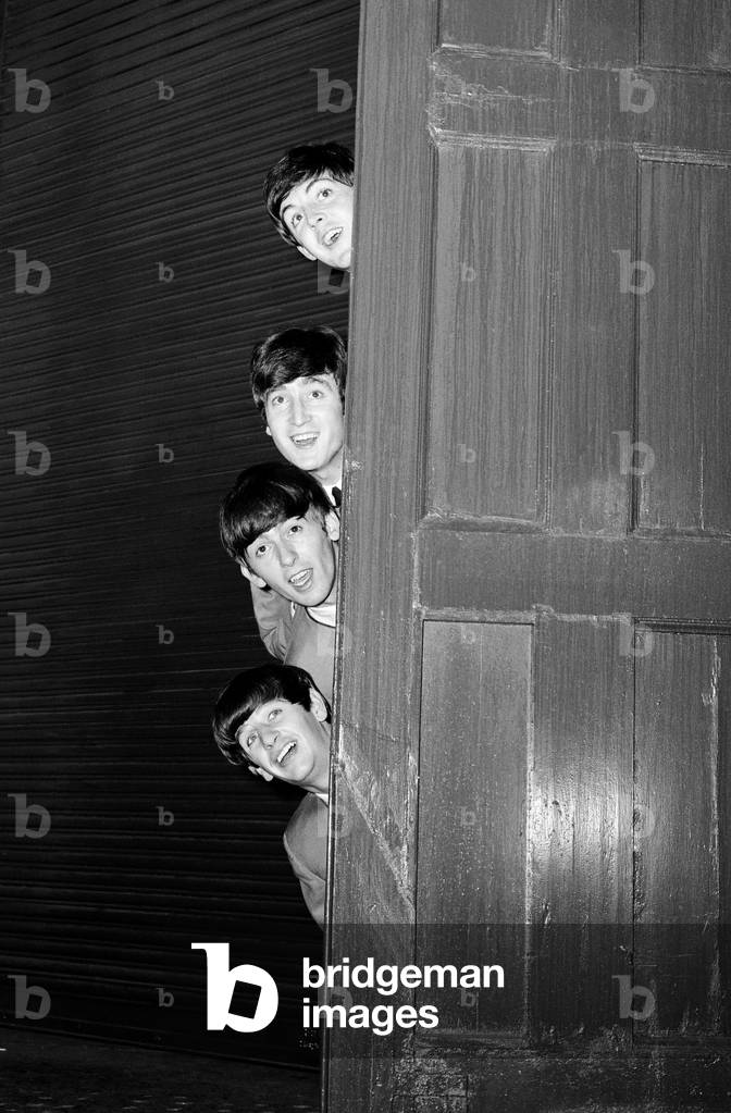 The Beatles peering out from behind a door. before the groups appearance at Sunday Night at the London Palladium, 13 October 1963 (b/w photo)