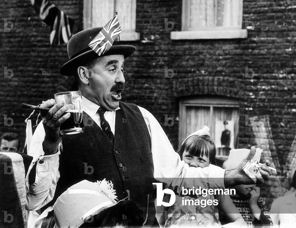 Warren Mitchell Actor as Alf Garnet - July 1968 in the TV programme Till Death Do Us part Wearing a bowler hat with a Union Jack in it, holding a drink and a cigar, talking and gesturing in a drunken manner, July 1968 (b/w photo)