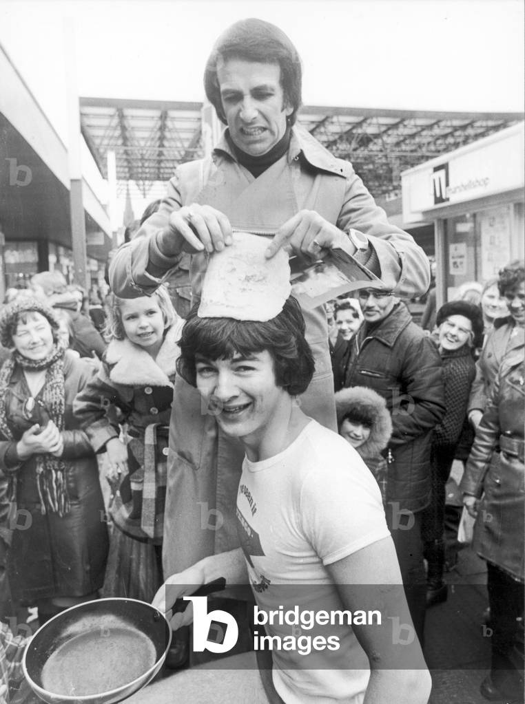 Paul Irvine, trainee manager at Tesco's, found himself trying his pancake as a hat when Birmingham comedian and actor Don Maclean presented him with his prize for winning the mens Pancake Race, Sandwell Mail, Birmingham, 22nd February 1977 (b/w photo)
