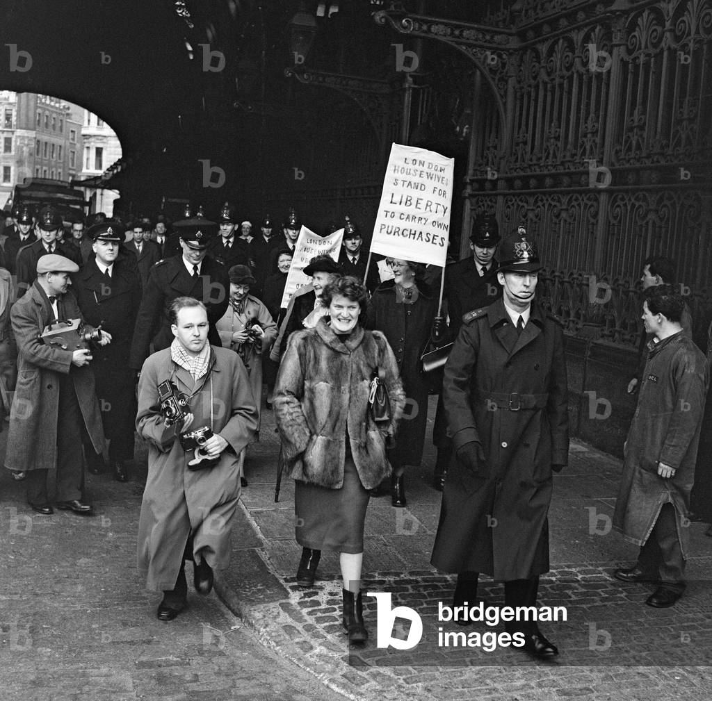 The London Housewives League sent a delegation to Smithfield Meat Market where they were ushered by City Police into the market superintendent's office. A large crowd of market workers waited outside the office singing and cheering. 20th January 1956 (b/w photo)
