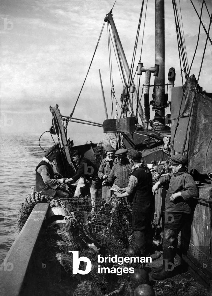 A Peaceful Scene - but there is danger below and above Deep Sea fishermen pause somewhere in the North Sea to mend their nets which have been damaged whilst trawling. Their nets were ripped over the wreck of a boat on sea bed. May 1942 P012253