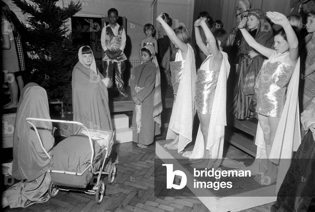A Hippie street singer, and Mary pushing a pram, were part of a school's Christmas pageant put on by the children of St. James' Norland School, Penzanza Place, Notting Hill. Angels bless Mary and baby, Hippie singer and Joseph watching. December 1969