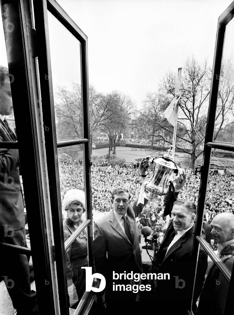 Tottenham Hotspur captain Danny Blachflower and manager Bill Nicholson hold the FA Cup trophy aloft to a crowd of fans as the team arrives home after defeating Burnley 3-1 in the FA Cup Final at Wembley. May 1962 (photo)
