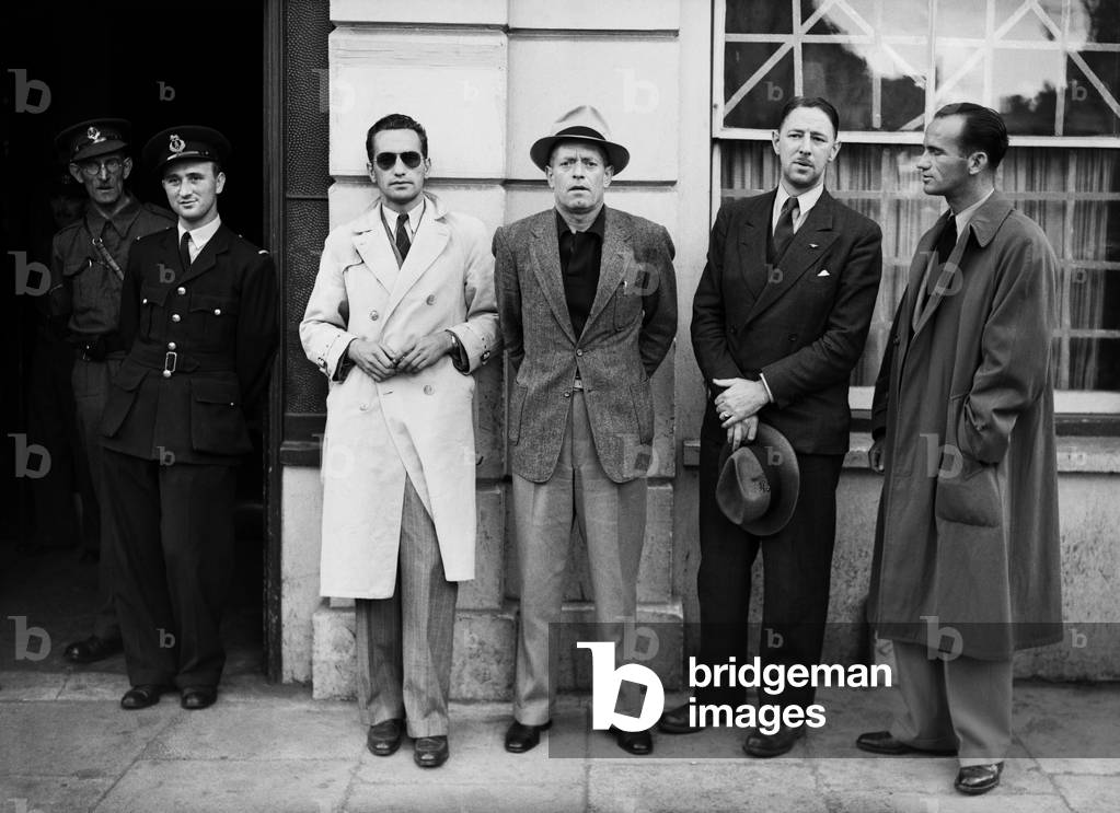 One of the BOAC flying boat crew poses with passengers at Poole police station where travel documents are checked before boarding a flight at Poole in Dorset, c. 1940 (b/w photo)
