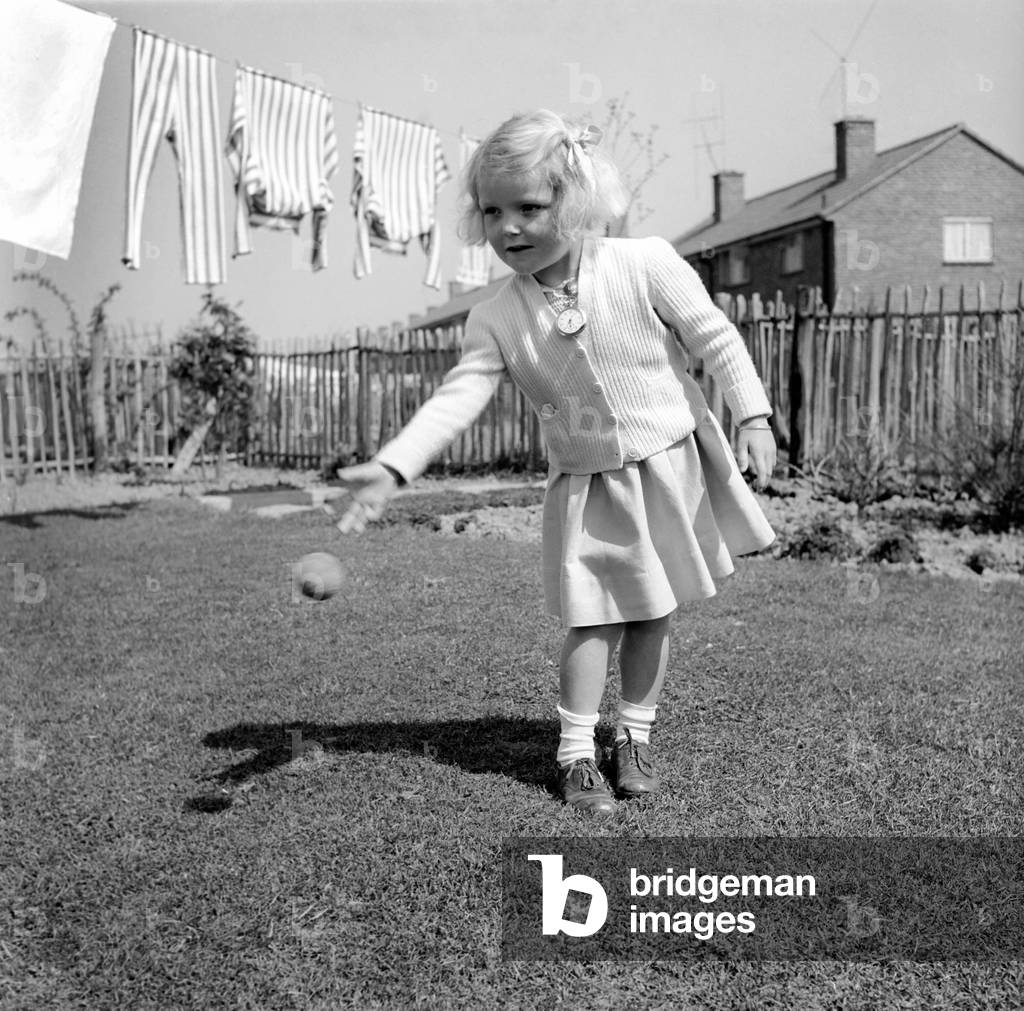 Small girl playing in the garden of her home with a ball, 1954 (b/w photo)